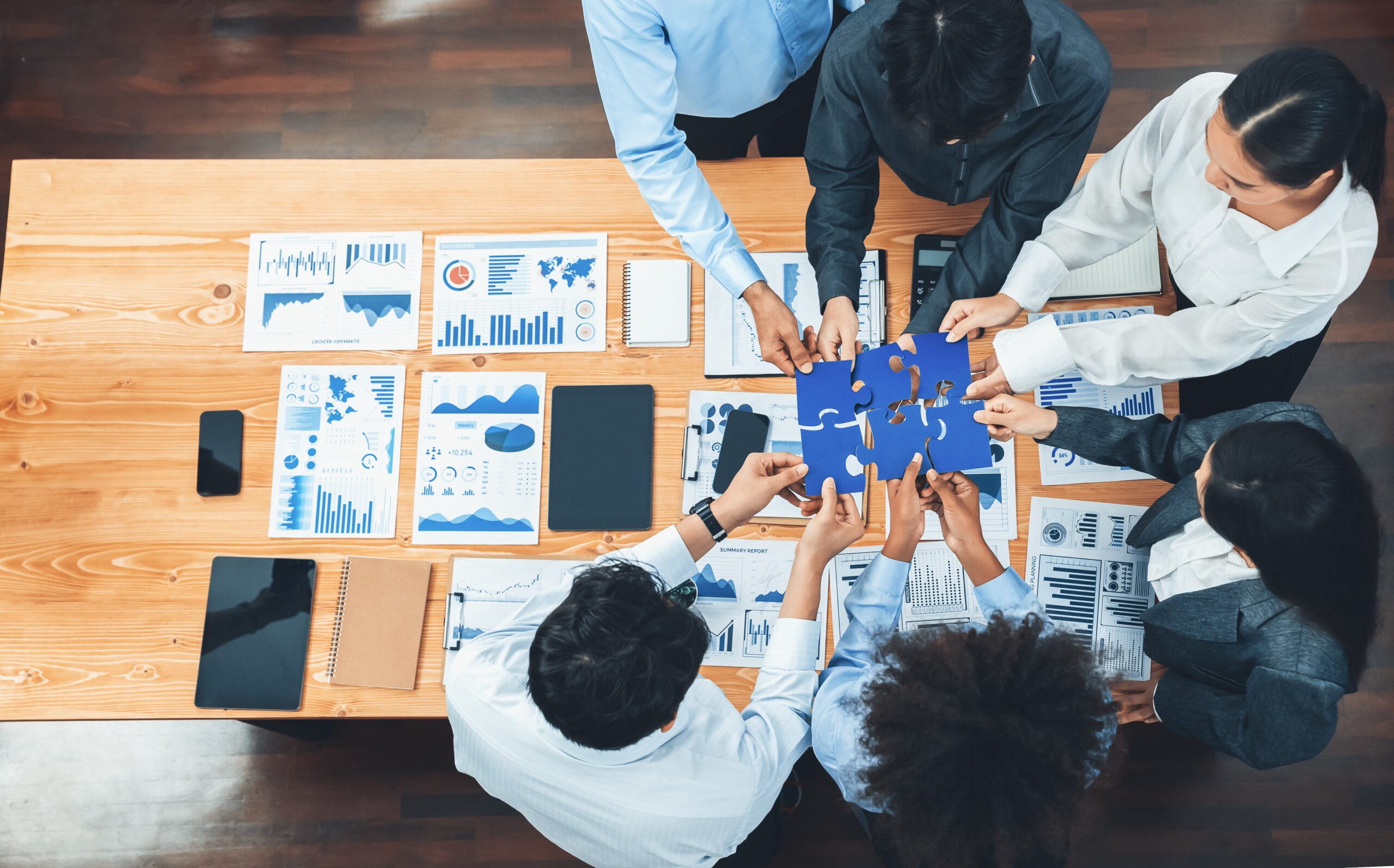 Mehrere Personen arbeiten gemeinsam an einem Tisch mit Diagrammen und Notizen, w&auml;hrend sie ein blaues Blatt betrachten.