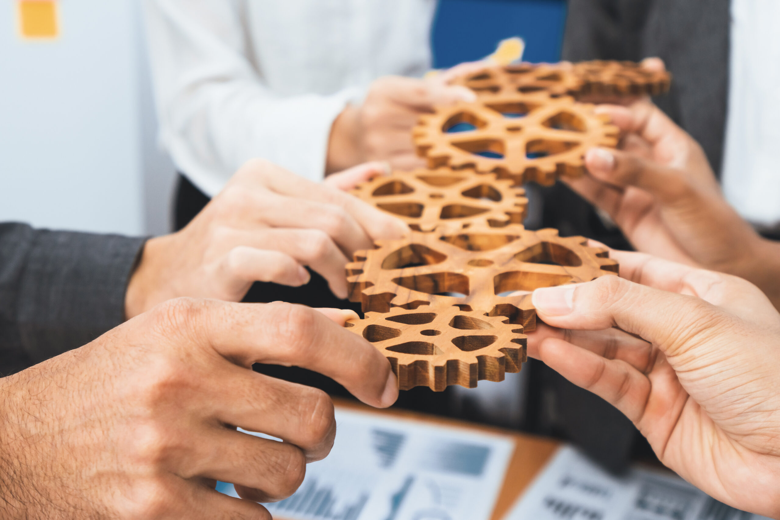 H&auml;nde halten mehrere h&ouml;lzerne Zahnr&auml;der, die Zusammenarbeit und Teamarbeit symbolisieren.